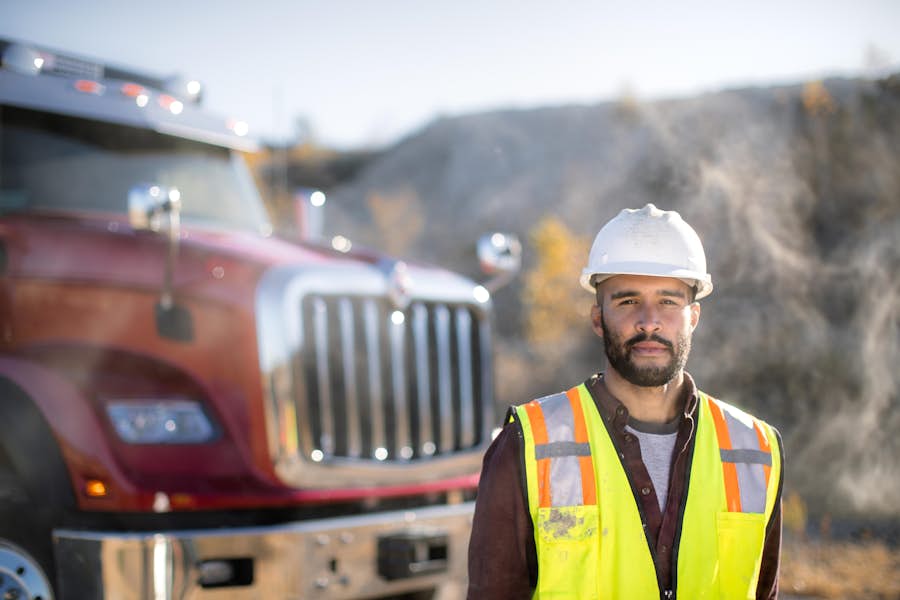 A person in a yellow vest and a hard hat standing in front of a truck