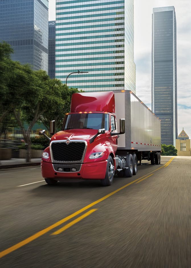 A red semi truck on a street with tall buildings in the background
