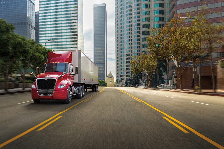 A red semi truck on a street with tall buildings in the background