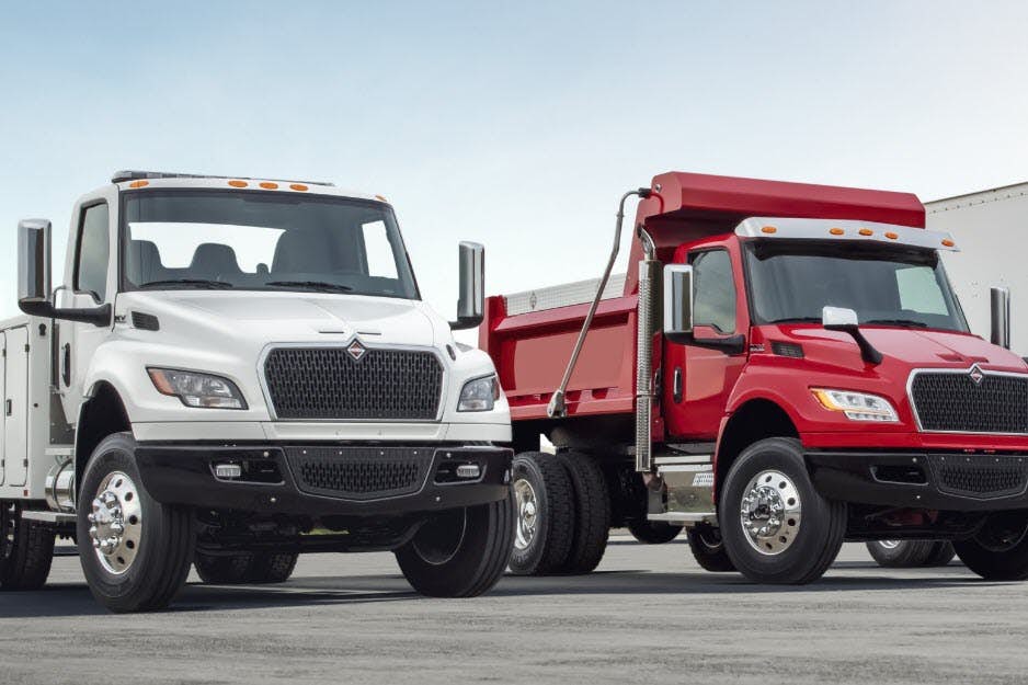 A red dump truck next to white truck