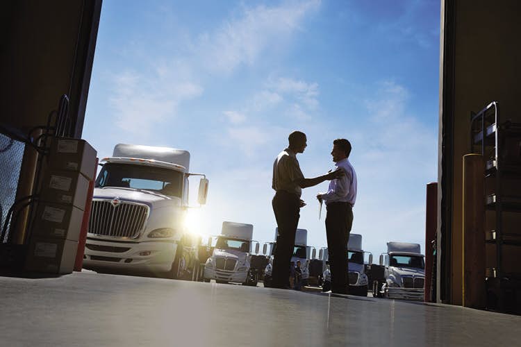 A couple of men shaking hands in front of semi trucks